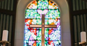 A cross in a church with a stained glass bokeh in the background