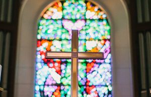 A cross in a church with a stained glass bokeh in the background