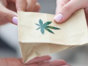 Marijuana In Colorado: Arrests Down, Tax Monies Up holding over paper bag with marijuana sign