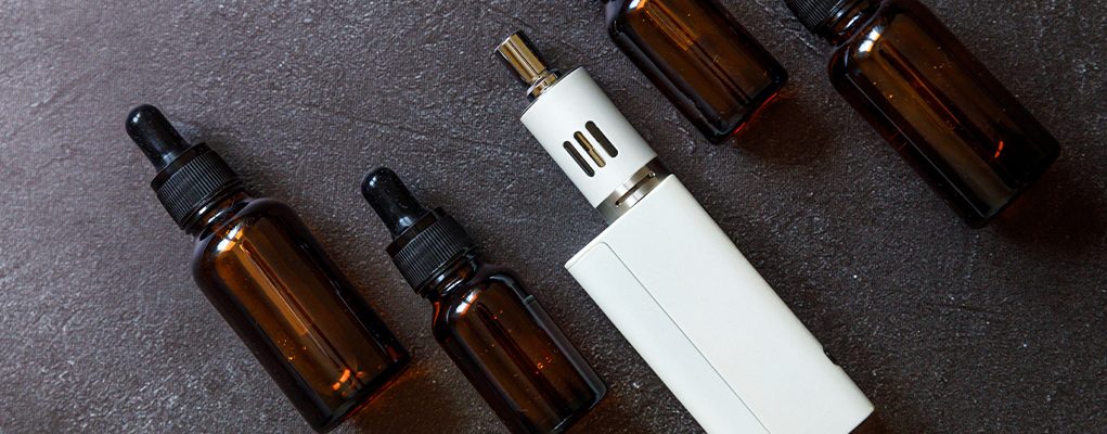 Vaping device e-cigarette electronic cigarette and liquid bottles on dark black stone shale background