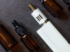 Vaping device e-cigarette electronic cigarette and liquid bottles on dark black stone shale background