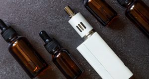 Vaping device e-cigarette electronic cigarette and liquid bottles on dark black stone shale background