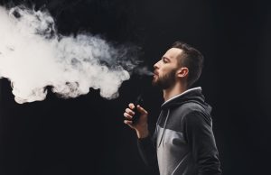 Young man vaping e-cigarette with vapour